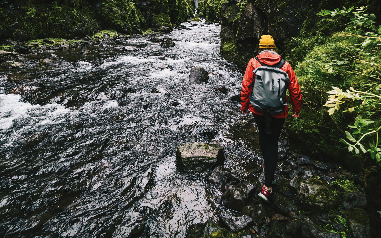 Escursionista con abbigliamento tecnico da montagna e zaino mentre attraversa un torrente nel bosco